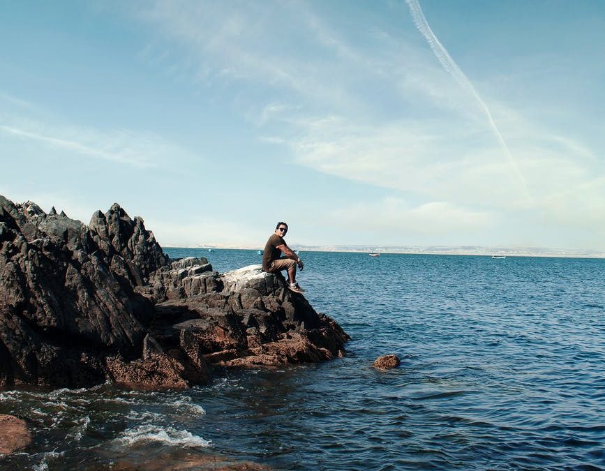 man in black jacket sitting on rock near sea